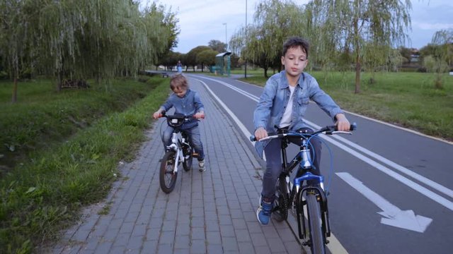Two caucasian boys in denim clothes ride bicycle