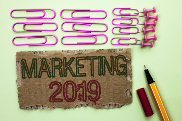 Handwriting text writing Marketing 2019. Concept meaning New Year Market Strategies Fresh start Advertising Ideas written Tear Cardboard Piece plain background Marker and Pins next to it.