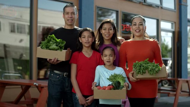 Portrait of a beautiful family, holding boxes of vegetables, standing in front of their family business