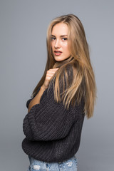 Portrait of a cheerful young woman in sweater smiling with arms crossed on gray background