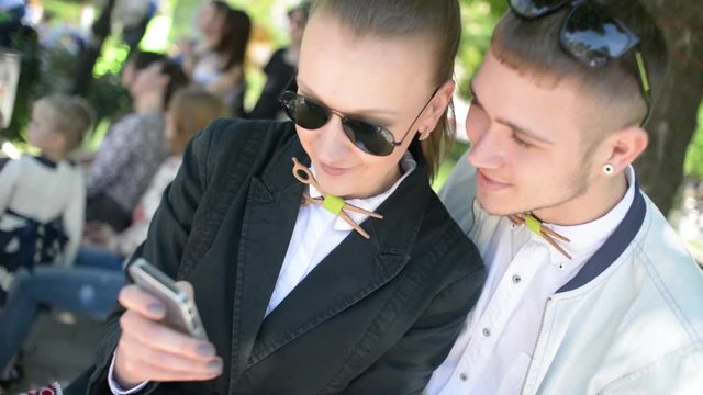 Beautiful young friends boy and girl browse photos on mobile phone in park