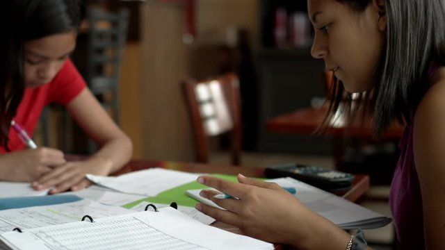 Two young teenage girls work on homework in their family's Mexican food restaurant 