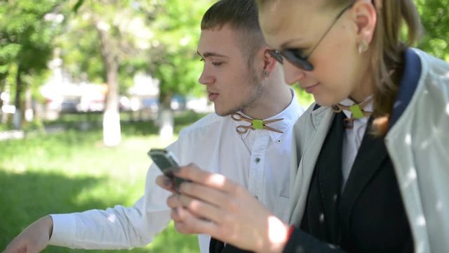 Beautiful young friends boy and girl browse photos on mobile phone in park
