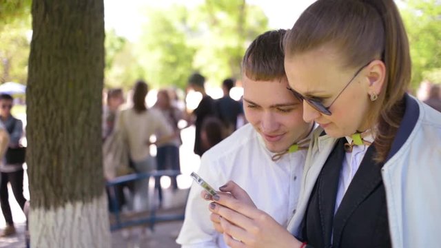 Beautiful young friends boy and girl browse photos on mobile phone in park