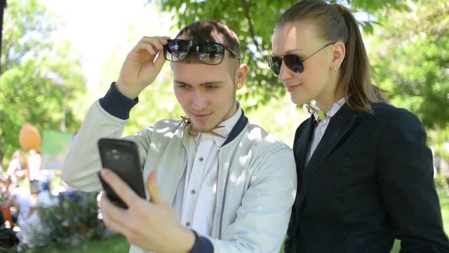 Beautiful young friends boy and girl browse photos on mobile phone in park