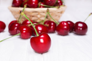 Ripe cherries in a wicker plate on a white wooden background