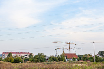 Peri urban scenery of the suburb of Belgrade, with cranes on a construction site in the middle of fields, and new apartment buildings visible in the background.