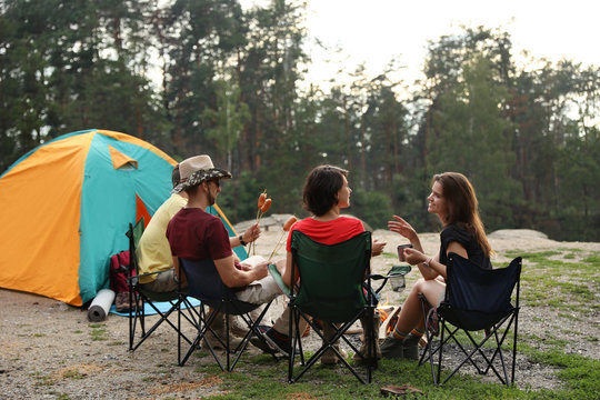 Young people having lunch with sausages near camping tent outdoors