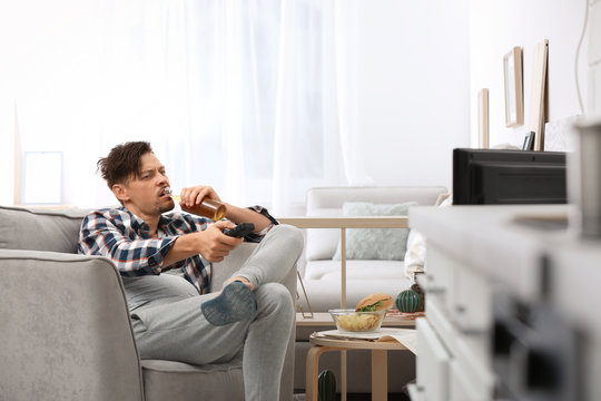 Lazy man with bottle of beer and chips watching TV at home