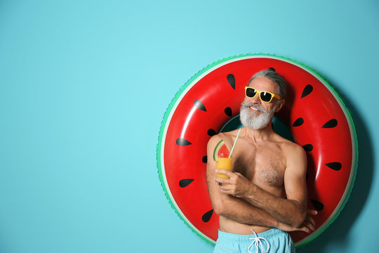 Shirtless man with inflatable ring and glass of cocktail on color background