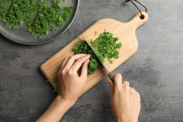 Woman cutting fresh green parsley on wooden board, top view