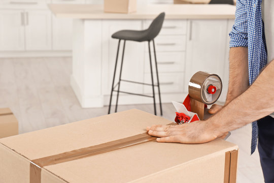 Man packing moving box indoors, closeup. Space for text