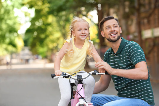 Father teaching daughter to ride bicycle on street