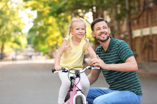 Father teaching daughter to ride bicycle on street