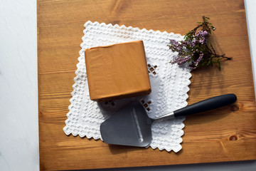 Fototapeta na wymiar Traditional Norwegian brown cheese on a white napkin with embroidery hardanger. Brunost. Sheep cheese. A piece of soft brown caramel cheese and a slicer on a wooden surface.