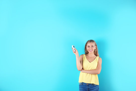 Young woman with air conditioner remote on color background, copy space text