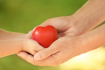 Adult and child hands holding heart on blurred background, closeup. Family concept