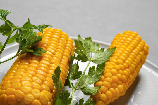Plate with ripe corn cobs and parsley on grey background, closeup
