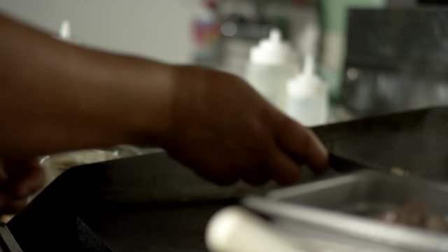 Close up of a woman scooping carne asada from a flat grill into a steel hotel pan in a Mexican food restaurant kitchen