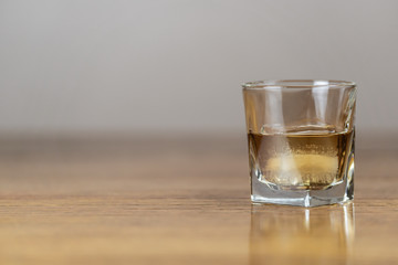 Whiskey in an elegant glass on the rocks with a large ice cube on a rustic wood table.