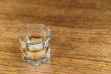 Whiskey in an elegant glass on the rocks with a large ice cube on a rustic wood table.