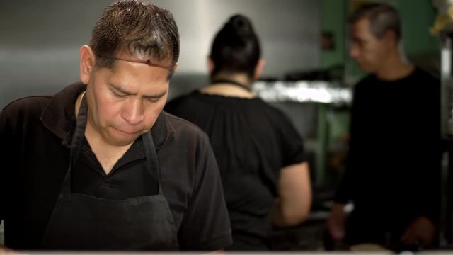 Cooks of hispanic descent preparing food in a Mexican food restaurant while the manager comes in to help them