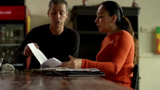 A couple of hispanic descent discuss bills and expenses in their family Mexican food restaurant