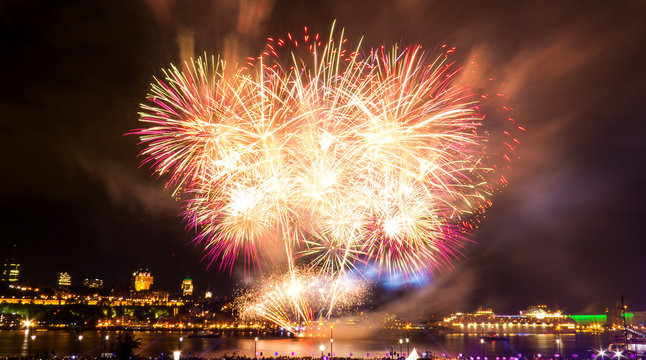 Orange, green, and pink fireworks over the Saint-Lawrence River near Quebec City during a Canadian summer festival.