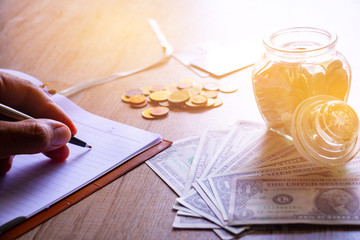 Close up hand man 's writing on note book with coin , dollar and Credit Cards.They are for save money and rays light. Photo finance and save money concept idea.
