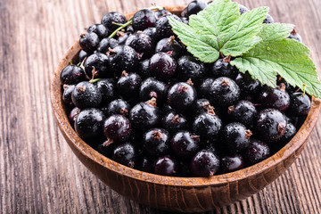 Big wooden bowl with fresh black currant and original leaves on wooden background close-up.