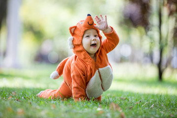 Happy baby girl dressed in fox costume crawling on lawn in park