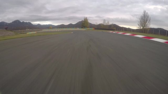 POV: Driving a fast car along the scenic asphalt racetrack on a cloudy evening. Breathtaking first person view of racing a supercar through the long turns of a modern circuit. Adrenaline joyride.