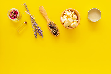 Hair treatment with natural products. Jojoba, argan, coconut oil near bunch of lavender and hairbrush on yellow background top view copy space