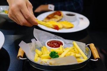 Hand holding a piece of french fried with tomato sauce
