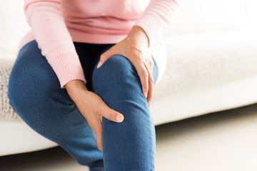 Closeup young woman sitting on sofa and feeling knee pain and she massage her knee at home....
