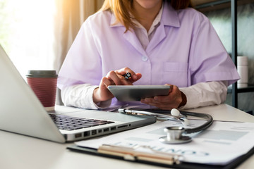 The doctor is working on a tablet and audio player and a digital tablet computer in a modern office with coffee in the morning at the desk.