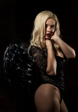 fallen black angel with wings. Sexual woman in black bodysuit and black wings on a black background.