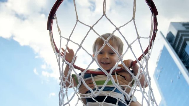 4k video of cute smiling toddler boy hanging on basketbal ring and looking inside