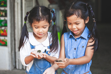 Two cute asian child girls holding and playing with black caterpillar with curious and fun together.