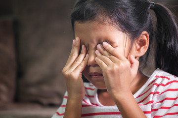 Sad asian child girl is crying and rubbing her eyes with her hands