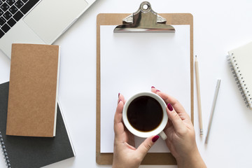 Naklejka premium Top view over the working desk with notebooks, calculator, cup of coffee in woman's hands, pen, pencil and laptop. Copy space for text. Flat lay of a workplace on white background