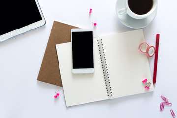 Top view over the working desk with notebooks, pen, paper clips, tapes, phone, tablet and a cup of coffee. Copy space for text. Flat lay of a workplace on white background