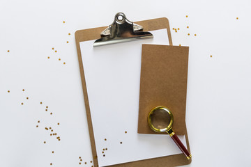 Top view over the working desk with paper, notebook and magnificent glass at the top with randomly droped golden stars. Copy space for text. Flat lay of a workplace on white background