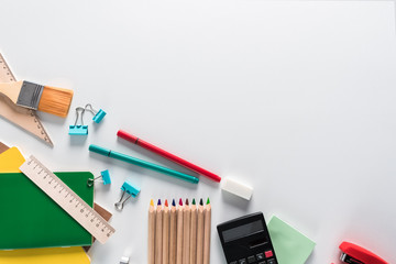 Top view over a notebooks, paints, pencils, rulers, paper clips, brushes, stepler, glue, sharpener, pens, paper on a white background. Back to school concept. Office supplies flat lay