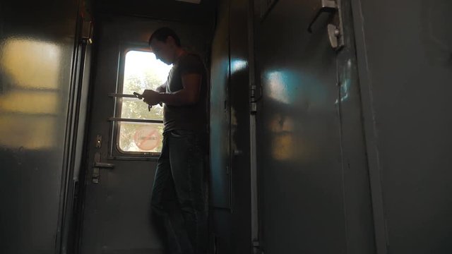 the man silhouette is standing on the train Railway carriage holding a smartphone and . slow motion video. man writes messages in the smartphone in the train social media. man with lifestyle
