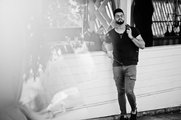 Stylish beard arabian man in glasses and black t-shirt smoking hookah outdoor. Arab model having rest.