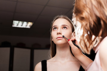 makeup artist dabbing the mixed foundation on a face of a young beautiful client. concept of...