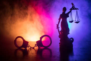 Legal law concept. Silhouette of handcuffs with The Statue of Justice on backside with the flashing red and blue police lights at foggy background.