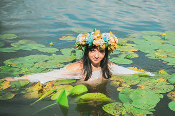 Obraz na płótnie Canvas Beautiful dark haired girl in white dress posing in river with water lilies. Fairytale story about modern ophelia 