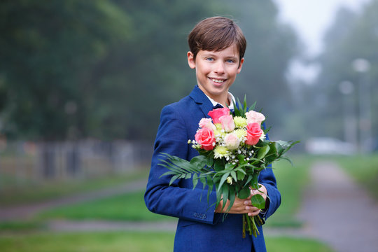 Cute school boy in dark classic suit holding bouquet of bright and colorful flowers